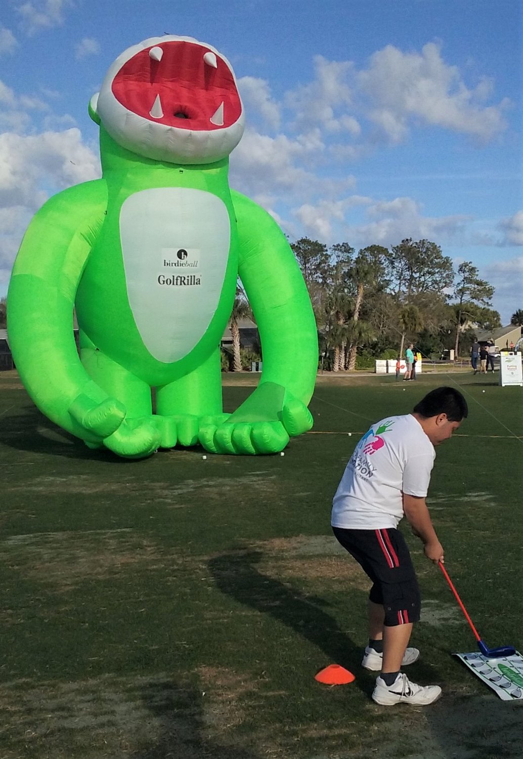 A young golfer attempts to hit a ring-shaped “golf ball” into the mouth of Golfrilla, a large, inflatable, green gorilla.